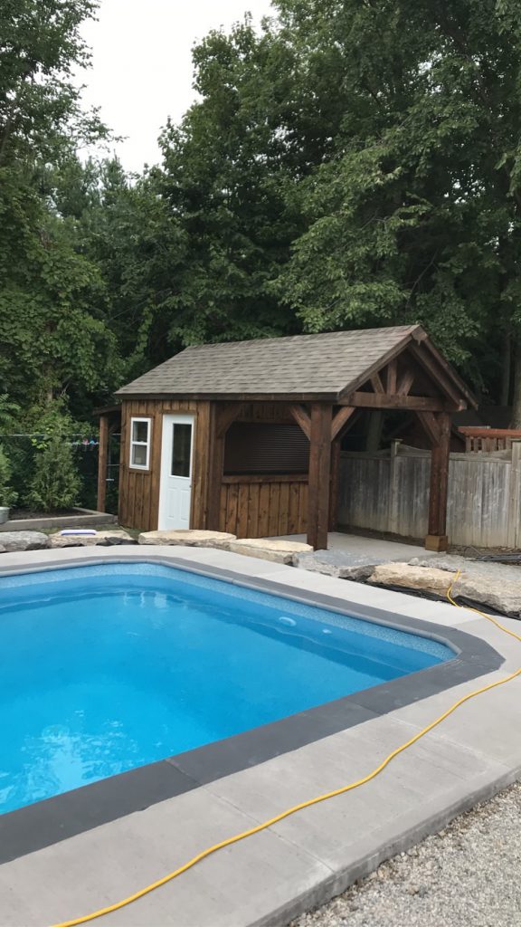 Pool cabana shed with covered porch and landscaping next to a pool